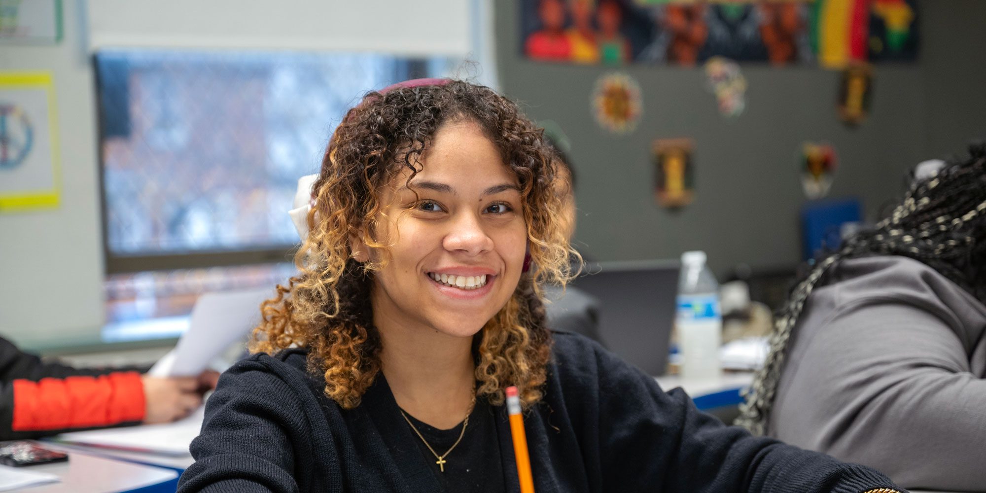Smiling student holding a pencil at a classroom desk.