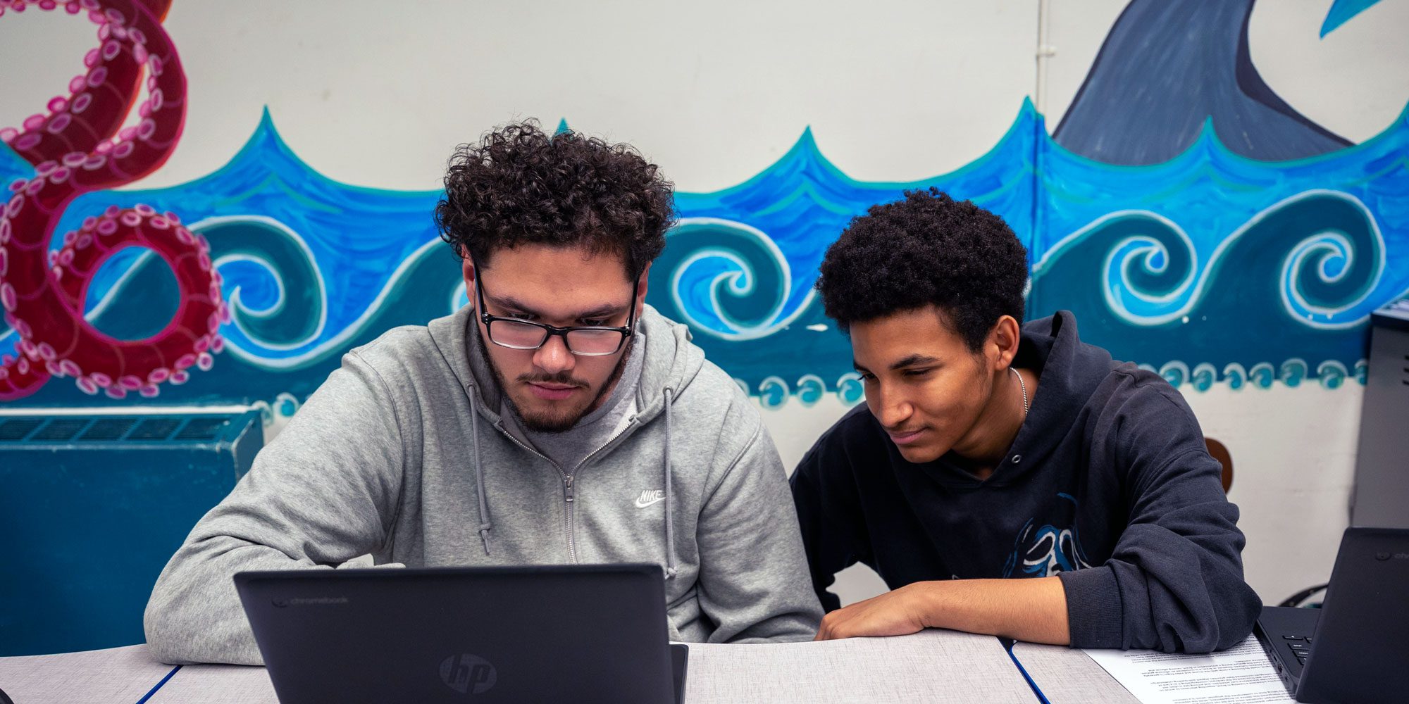 Two students working together on a Chromebook in a classroom.